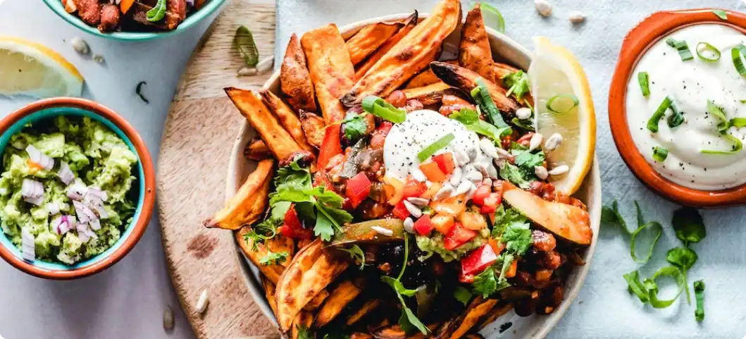 Sweet potato fries with sour cream, tomatoes, herbs, and seeds beside guacamole—ideal snack after using industrial powder mixers.